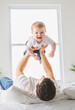 © Louis-Paul Photo - young father with a baby boy having fun with his son close to a window on bed