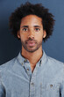 © Katie/peopleimages.com - Young man, portrait or confident in studio as creative professional or casual fashion by blue background. Brazil person, face and afro for ambition as designer and trendy clothes or relax in closeup