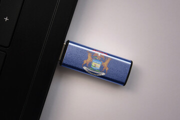 Wall Mural - usb flash drive in notebook computer with the national flag of michigan state on gray background.