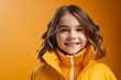 portrait of a smiling little girl in a yellow jacket on an orange background