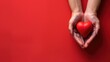 Hands cradling a red heart on a solid red background, symbolizing care, love, and health