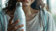 A close-up of a hand holding a reusable water bottle, with details of the bottle's design, the water droplets on the bottle, and the person's smile.
