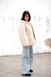 © Вероника Зеленина - A beautiful girl with a stylish bob haircut is walking around the city,  against the background of grey wall. The woman is wearing a white faux fur sheepskin coat and jeans