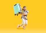 Fototapeta Natura - Full body photo of a funny young happy man in sunglasses carrying his blue suitcase is going on summer holiday trip and having fun on a yellow background. Vacation and travel concept.