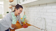 Young upset screaming woman in gloves trying to unclog sink drain standing in the kitchen. Tired girl cleaning pipe with a cup plunger at home. Housekeeping and household work concept. Banner.