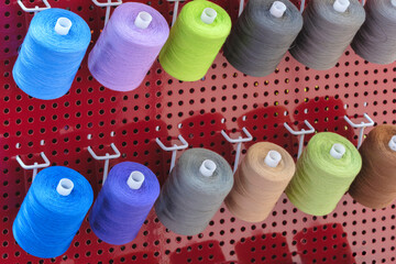 Aufkleber - A row of colorful spools of thread are displayed in a store. The spools are arranged in a rainbow pattern, with each color being represented in the display. The spools are of various sizes