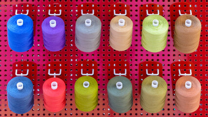 Aufkleber - A row of colorful spools of thread are displayed in a store. The spools are arranged in a rainbow pattern, with each color being represented in the display. The spools are of various sizes