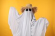 Person in ghost costume and straw hat on yellow background