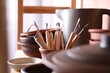 Set of different crafting tools and clay dishes on table in workshop, closeup