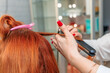 A skilled hairdresser creates beautiful curls for a happy redhead client in a trendy salon.