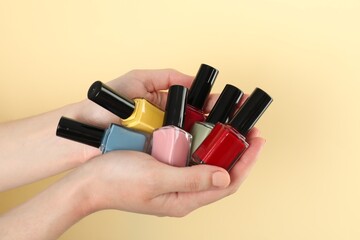 Wall Mural - Woman holding nail polishes on beige background, closeup