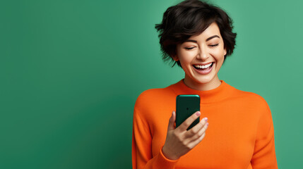 Wall Mural - Happy smiling young woman is using her smartphone against green background