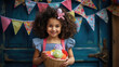 Young girl with curly hair is smiling joyfully in front of a blue background adorned with colorful party bunting
