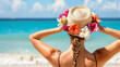 A woman wearing a straw hat adorned with flowers stands in a bikini on the beach, gazing at the turquoise sea.