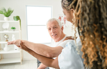 Wall Mural - Black physiotherapist helping senior man with in clinic. Elderly man undergoing physiotherapy treatment for injury