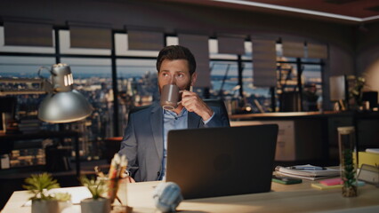 Wall Mural - Overworked man sipping coffee at night room closeup. Businessman looking laptop