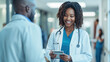 © Studio Nova - Smiling young female doctor with a stethoscope around her neck, holding a tablet, standing in a hospital corridor.
