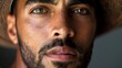 © irina - Close-up of a young man with striking facial features and a hat, showcasing intricate details of his skin and intense gaze in a soft-lit environment