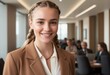 A happy professional stands in a modern office setting. Her braided hair and beige blazer project a friendly yet businesslike image.