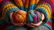 a close up of two balls of yarn in a person's hands with a multicolored afghan in the background.
