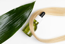 A Sleek Green Dropper Bottle Of Natural Hair Oil Lies Against A Lock Of Blonde Hair, With A Large, Lush Green Leaf Creating An Organic Feel