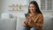 © Yuliia - Asian chinese korean businesswoman woman girl freelancer work from home in kitchen read good news smiling use mobile phone choose goods on internet order delivery online typing message cellphone chat