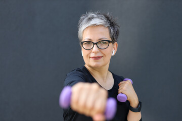 Wall Mural - A mature Caucasian woman embraces fitness, exercising with dumbbells outdoors, radiating health and vitality.