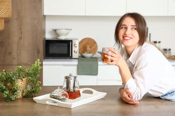 Sticker - Young woman with glass cup of tea in kitchen