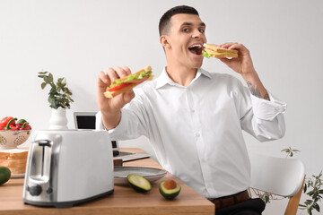 Canvas Print - Young man eating tasty sandwiches made from toasts in kitchen