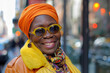 A woman wearing sunglasses and an orange turban smiles for the camera
