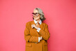 © Asya Molochkova/Stocksy - Cheerful senior woman in yellow jacket on pink studio background