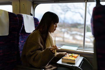 Asian woman eating traditional Japanese pork cutlet with rice Tonkatsu in lunch box bento during travel on train. Attractive girl travel Japan on railroad transportation on winter holiday vacation.