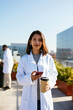 © BONNINSTUDIO/Stocksy - Doctor with coffee to go holding smartphone