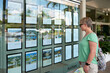 © Rowena Naylor/Stocksy - Woman looking at properties for sale in Real Estate window