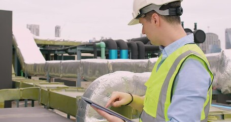 Canvas Print - Engineer inspecting insulated pipelines at an industrial site with a digital tablet.