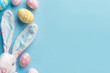 Top view photo of easter bunny ears white pink blue and yellow eggs on isolated pastel blue background with copyspace in the middle Easter party concept.