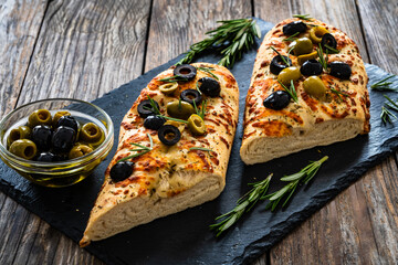 Wall Mural - Focaccia alle olive - baked sandwich with green and black olives and rosemary on wooden background
