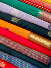 Wall Mural - Closeup view of stacked saris or sarees in display of retail shop, for use as indian textiles background.