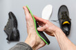 Close up of man hands fitting orthopedic insoles on a gray background.