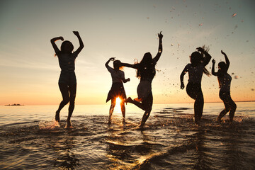 Wall Mural - Silhouettes of happy girls are having fun and dancing at sunset lake beach