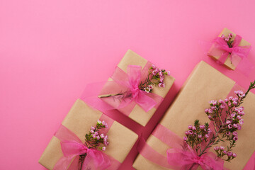 Wall Mural - Craft brown gift box with pink ribbon and waxflowers on pink background