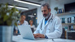 © safu designe - Male mature doctor in white coat sitting at the table working on laptop with his female colleagues nurses at office