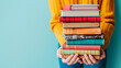 © safu designe - Woman hands holding pile of books over light blue background. Education, library, science, knowledge, studies, book swap, hobby, relax time
