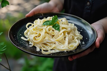 Wall Mural - Hand-Held Black Plate Showcasing Creamy Fettuccine Alfredo