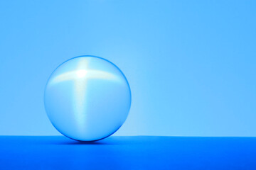 Sticker - Transparent glass ball on table against light blue background. Space for text