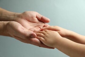 Wall Mural - Father and child holding hands on light blue background, closeup