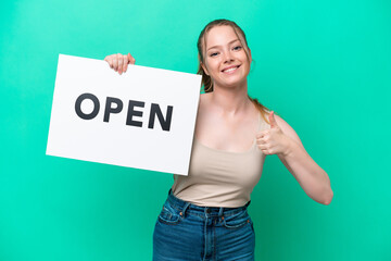 Wall Mural - Young caucasian woman isolated on green background holding a placard with text OPEN with thumb up