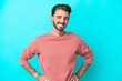 © luismolinero - Young caucasian man isolated on blue background posing with arms at hip and smiling