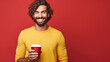 © Studio Nova - Cheerful man with a beard and eyeglasses, holding a to go coffee cup, with a joyful expression against a vibrant red background.