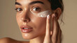 © MP Studio - Close-up of a woman with clear blue eyes and flawless skin applying a white cream on her cheek with her fingers, exemplifying a skincare routine.